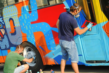 Graffiti artists work on decorating a bus during a festival promoting local transportation.